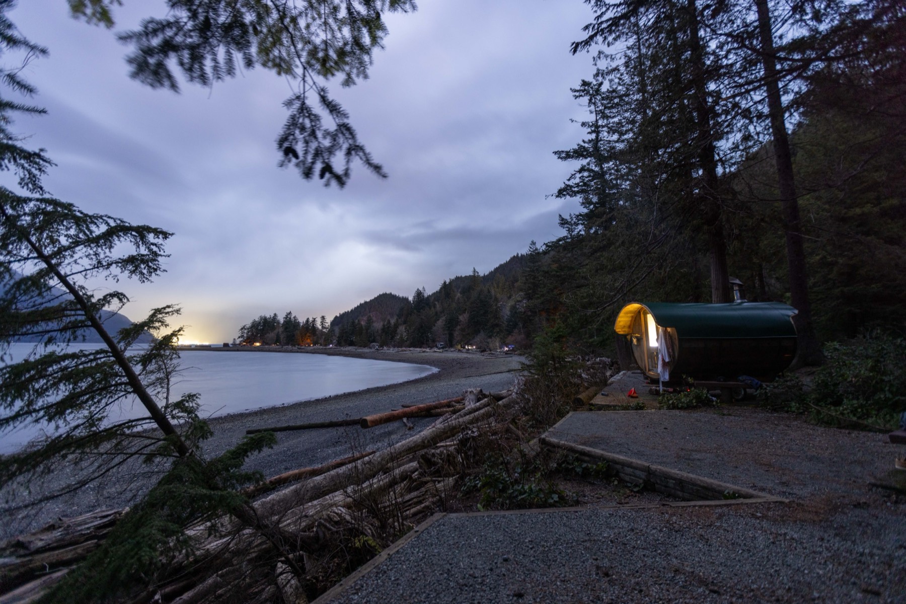The barrel sauna glowing at dusk beside the water
